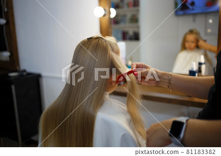hairdresser straightens hair of a little girl in a beauty salon 81183382
