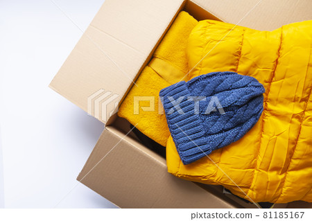 Warm yellow jacket and blue knitted cap in the opened cardboard box. Fashion outfit. Bright colors. Home storage. 81185167