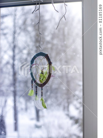 Handmade dream catcher on window background in winter day. Tribal decorative design element. Beads and feathers 81185169