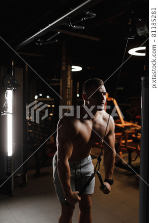 guy bodybuilder model with a naked torso, trains in the gym. The muscles are tense. Dark background. guy bodybuilder model with a naked torso, trains in the gym. The muscles are tense. Dark background. 81185281