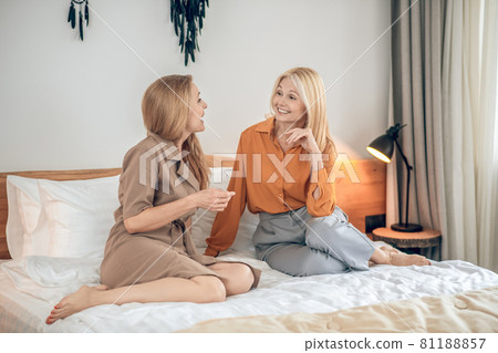 Two smiling women sitting on the bed and looking photos on internet 81188857