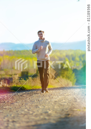 Man jogging in rural nature at beautiful summer day. Sport fitness model caucasian ethnicity training outdoor. 81189366