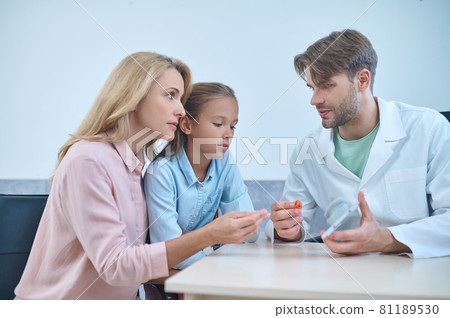 Male doctor demonstrating a deaf aid to his female patients Male doctor demonstrating a deaf aid to his female patients 81189530