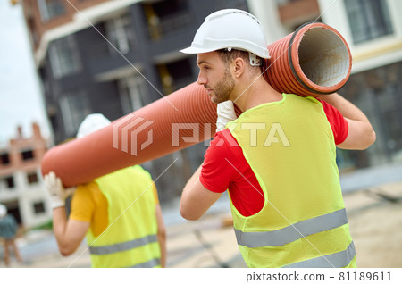 Two workers in protective helmets carrying a corrugated drain pipe Two workers in protective helmets carrying a corrugated drain pipe 81189611