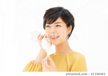 Young woman trying to put on a mask in front of a white curtain Young woman trying to put on a mask in front of a white curtain 81190463