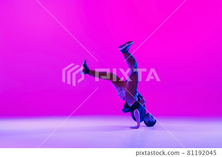 Young stylish man, hip-hop dancer dancing solo in modern clothes isolated over bright magenta background at dance hall in neon light. 81192045