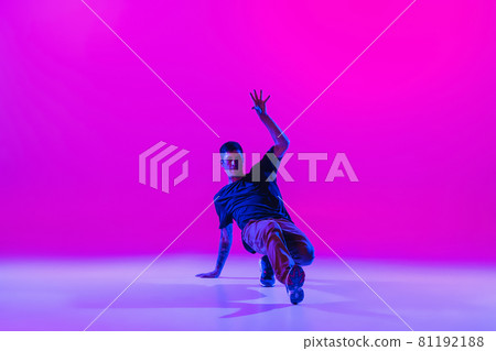 Young stylish man, hip-hop dancer dancing solo in modern clothes isolated over bright magenta background at dance hall in neon light. 81192188