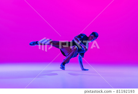 Young stylish man, hip-hop dancer dancing solo in modern clothes isolated over bright magenta background at dance hall in neon light. 81192193
