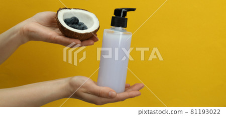 Female hands hold shower gel, coconut and blueberry on yellow background Female hands hold shower gel, coconut and blueberry on yellow background 81193022