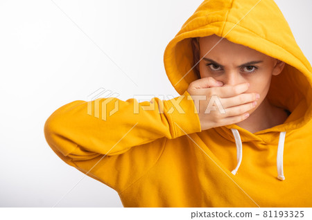Young woman in ocher hood covers her face with hand on white background. Young woman in ocher hood covers her face with hand on white background. 81193325