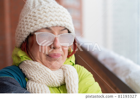 Portrait of a red-haired Caucasian woman in a white knitted hat and icy glasses outside in the frost 81193327