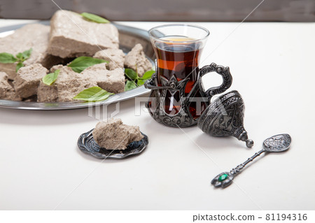 Turetius a glass of tea, a metal spoon and sunflower halva with almonds and pistachios stands on a wooden background. Turetius a glass of tea, a metal spoon and sunflower halva with almonds and pistachios stands on a wooden background. 81194316