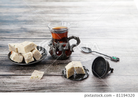 Turetius a glass of tea, a metal spoon and sunflower halva with almonds and pistachios stands on a wooden background. Turetius a glass of tea, a metal spoon and sunflower halva with almonds and pistachios stands on a wooden background. 81194320