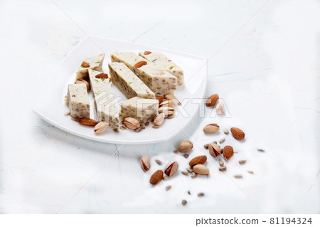 Halva made from sunflower seeds, almonds and pistachios lies on a plate on a white background. Copy spaes. Halva made from sunflower seeds, almonds and pistachios lies on a plate on a white background. Copy spaes. 81194324