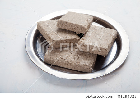 Halva from sunflower seeds in briquettes in a metal plate stands on a white background. Halva from sunflower seeds in briquettes in a metal plate stands on a white background. 81194325