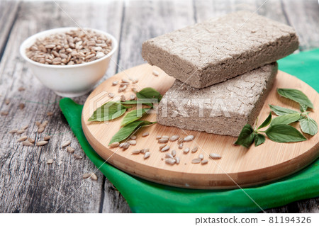 Briquettes of sunflower halva, sunflower seeds and green leaves lie on a wooden board on a green napkin.. A cup of honeycomb sunflower seeds nearby. Briquettes of sunflower halva, sunflower seeds and green leaves lie on a wooden board on a green napkin.. A cup of honeycomb sunflower seeds nearby. 81194326