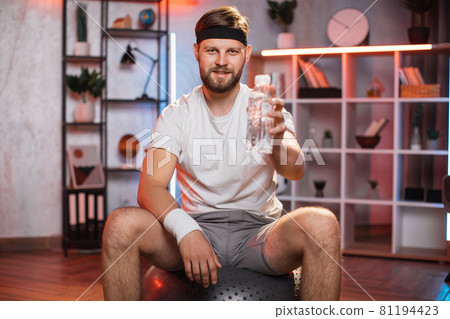 Smiling man holding bottle of water while sitting on fitball Smiling man holding bottle of water while sitting on fitball 81194423