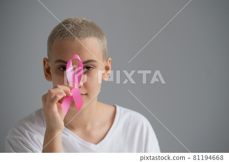 Young woman with short hair wearing a white t-shirt holding a pink ribbon as a symbol of breast cancer on a white background. Young woman with short hair wearing a white t-shirt holding a pink ribbon as a symbol of breast cancer on a white background. 81194668