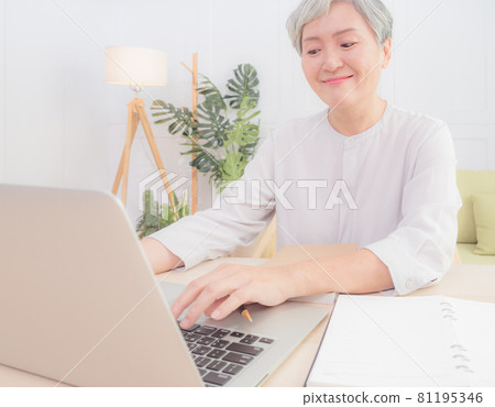 一位亞洲成熟女性在家中使用電子計算機寫作。 一位亞洲成熟女性在家中使用電子計算機寫作。 81195346