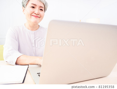 A mature woman in Asia uses an electronic computer to write at home. 81195358
