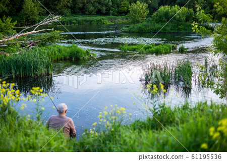 old man fishing with friend on a river at summer daytime with selective focus 81195536