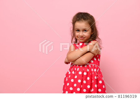 Beautiful preschool 4 years kid girl shyly hugging herself, cute smiling posing on camera against pink wall background with copy space. Confident portrait of shyly gorgeous baby girl. Adorable child Beautiful preschool 4 years kid girl shyly hugging herself, cute smiling posing on camera against pink wall background with copy space. Confident portrait of shyly gorgeous baby girl. Adorable child 81196319