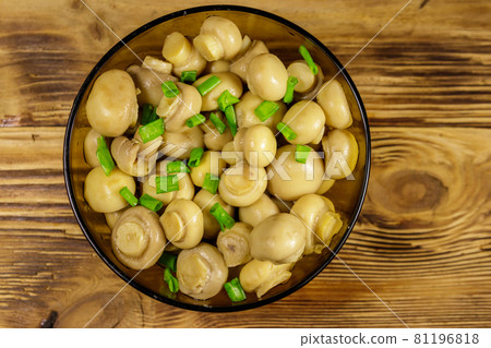 Glass bowl with pickled champignons. Marinated mushrooms on wooden table 81196818