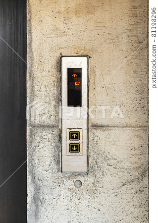 Call buttons for an elevator, complete with a floor indicator, against the backdrop of weathered concrete. 81198296