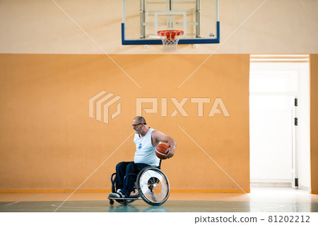 a war invalid in a wheelchair trains with a ball at a basketball club in training with professional sports equipment for the disabled. the concept of sport for people with disabilities 81202212