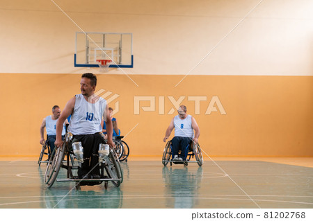 Disabled War veterans mixed race opposing basketball teams in wheelchairs photographed in action while playing an important match in a modern hall.  81202768