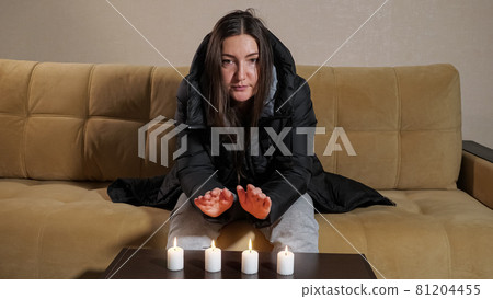Unhappy woman in warm jacket tries heat palms over candles Unhappy woman in warm jacket tries heat palms over candles 81204455