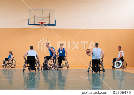 Disabled War veterans mixed race opposing basketball teams in wheelchairs photographed in action while playing an important match in a modern hall.  81206479