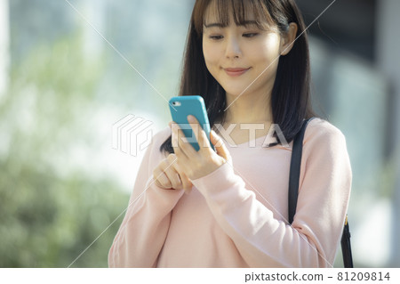 A woman looking at a smartphone outdoors 81209814