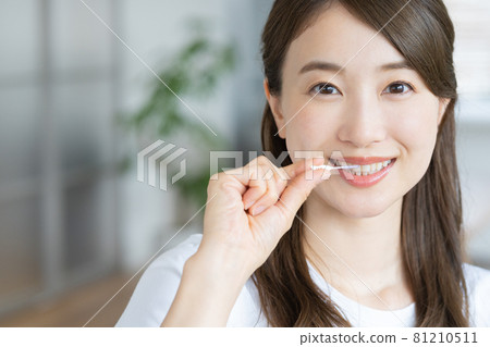 A young woman cleaning her teeth with an interdental brush in her living room A young woman cleaning her teeth with an interdental brush in her living room 81210511