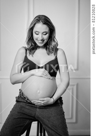 an attractive pregnant woman with a bare tummy on a chair. black and white photo 81210828