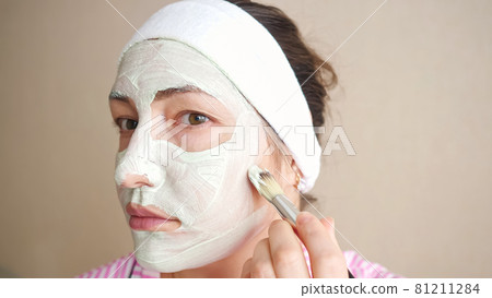 Woman applying a mask with a brush to face Woman applying a mask with a brush to face 81211284