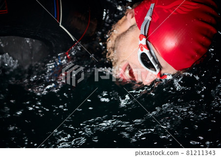 triathlon athlete swimming in dark night wearing wetsuit 81211343