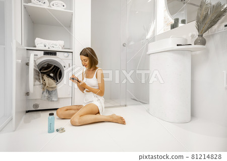Woman with cell phone preparing to wash clothes Woman with cell phone preparing to wash clothes 81214828