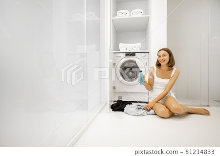 Woman washing clothes with washing machine in bathroom 81214833