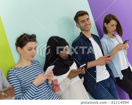 diverse teenagers use mobile devices while posing for a studio photo in front of a pink background 81214994