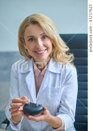 Woman in medical gown showing hearing aid 81217625