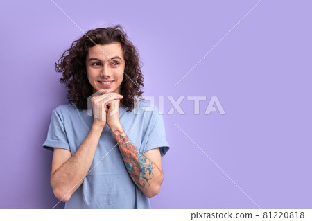 Young curly male in blue t-shirt, with a crafty expression that he came up with,keeping hands together Young curly male in blue t-shirt, with a crafty expression that he came up with,keeping hands together 81220818
