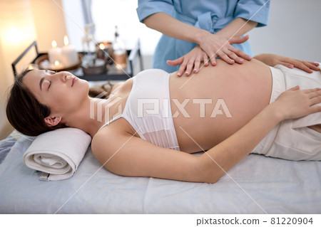 Pretty pregnant brunette lies on back at reception with massage therapist 81220904