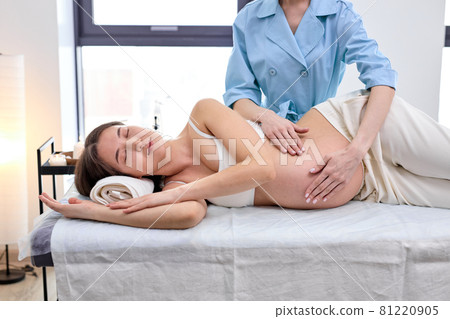 Pretty pregnant brunette lies on her side at reception with massage therapist Pretty pregnant brunette lies on her side at reception with massage therapist 81220905