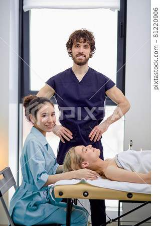 Two caucasian masseurs practice massaging on female client face and head Two caucasian masseurs practice massaging on female client face and head 81220906