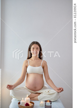 Attractive young pregnant woman sitting in yoga position in spa room, relaxing Attractive young pregnant woman sitting in yoga position in spa room, relaxing 81220914