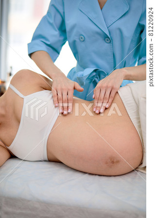 Female hands of massage therapist making light massage to the belly of pregnant 81220924
