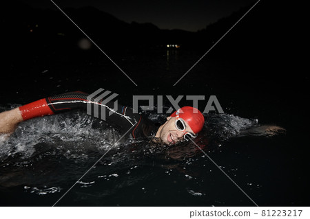 triathlon athlete swimming in dark night wearing wetsuit 81223217