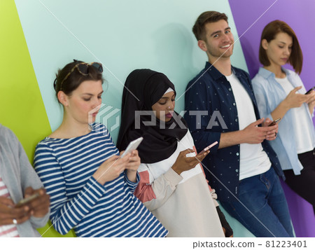 diverse teenagers use mobile devices while posing for a studio photo in front of a pink background 81223401