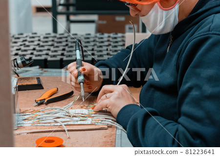 Industrial worker wearing a face mask due to a coronavirus pandemic solders cables from factory production equipment Industrial worker wearing a face mask due to a coronavirus pandemic solders cables from factory production equipment 81223641